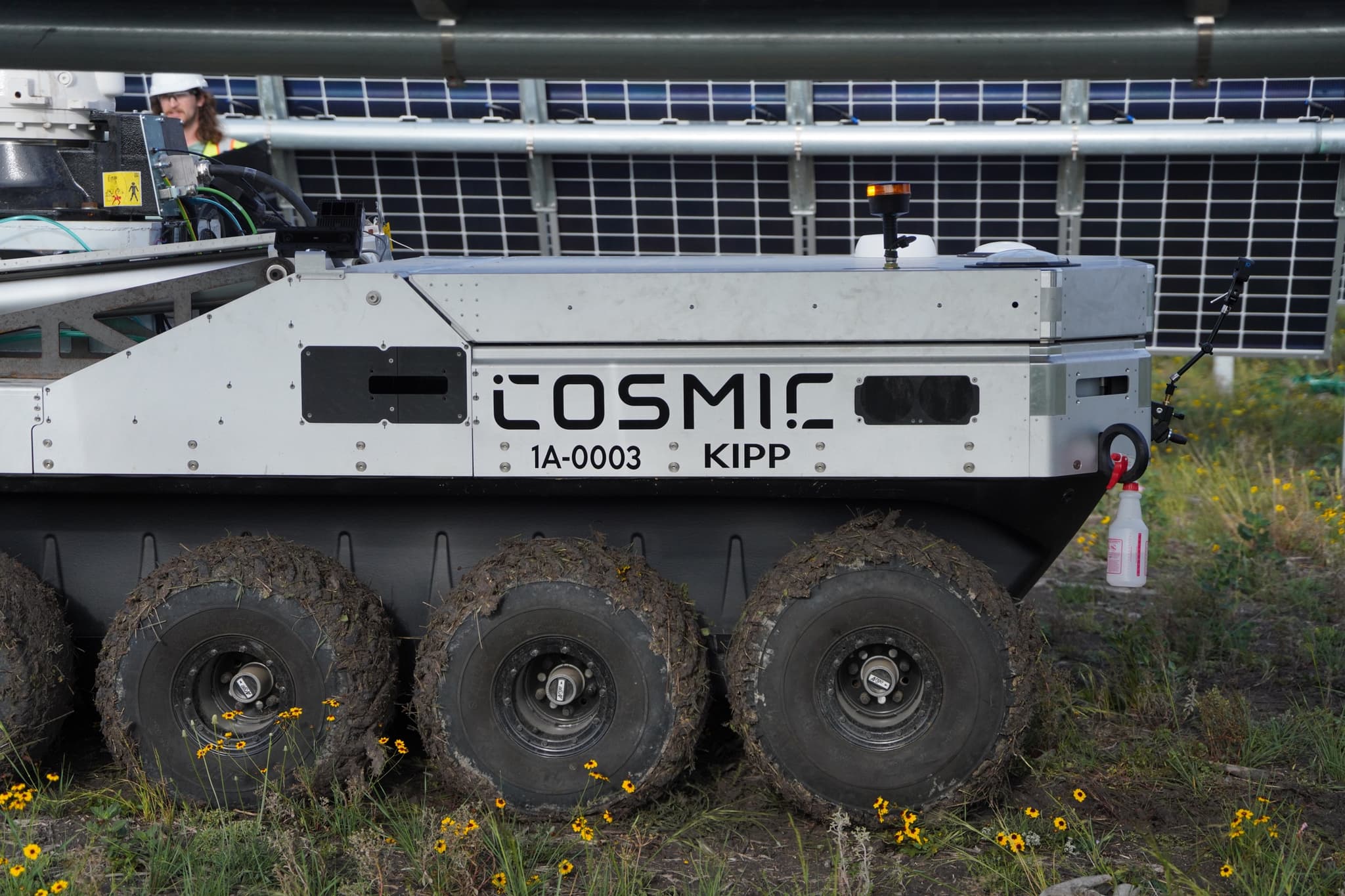 Cosmic-1 robot driving through wildflowers between solar rows
