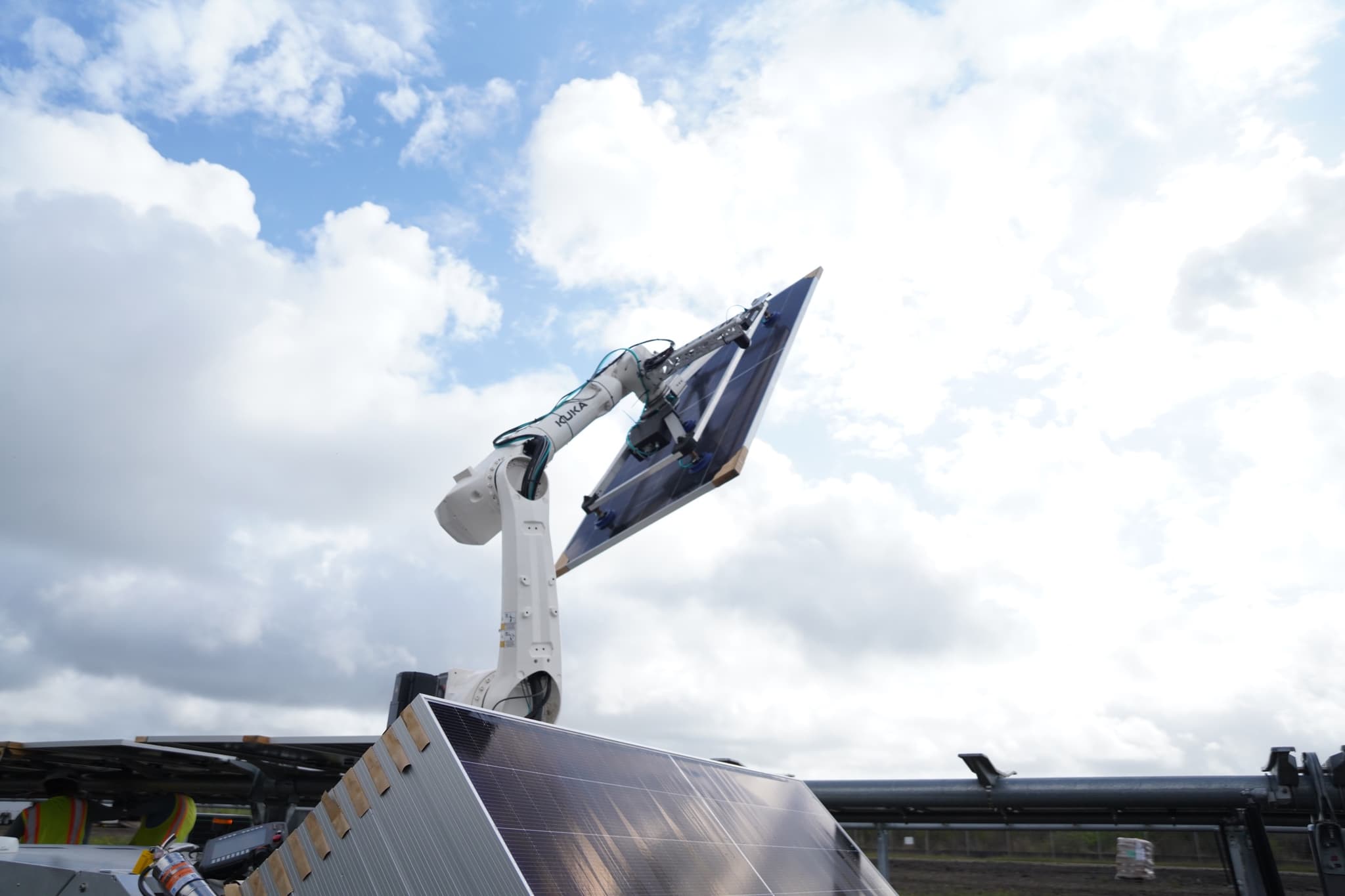 Cosmic-1 robotic arm lifting a solar panel against a cloudy Southern Texas sky